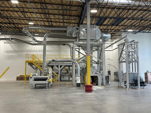 A complete scrap handling and dust collection system installed in a new corrugated plant, with the filter on its access platform, overhead duct runs, shredder, baler and separator tower