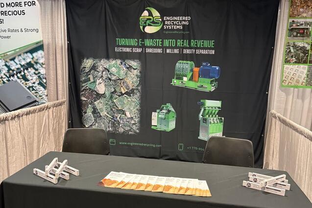 The ERS booth at the E-Scrap Conference in New Orleans, with the black ERS banner reading "Turning e-waste into real revenue — electronic scrap, shredding, milling, density separation" above a table in an ERS cloth, laid out with literature and giveaways.