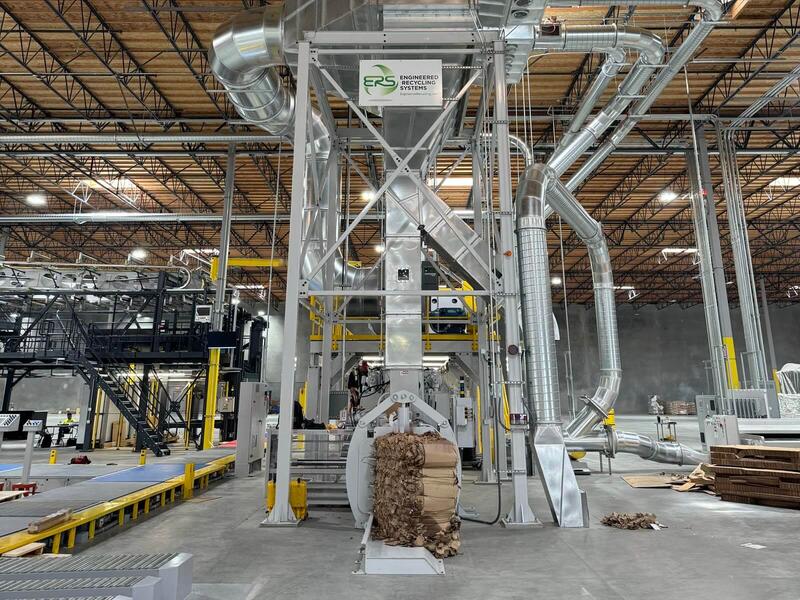 ERS-branded separator on a full-height steel tower with spiral duct runs feeding it, a baler at its foot producing a finished bale of trim, and a converting line on its mezzanine to the left