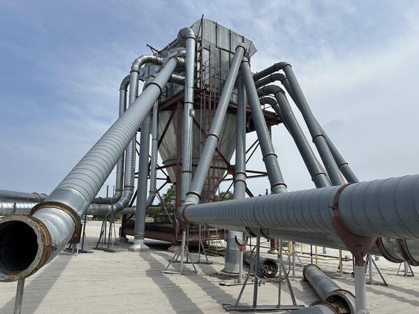 New duct runs tied into an existing rooftop cyclone at a corrugated plant, part of a dust control system installed in phases while the plant kept running