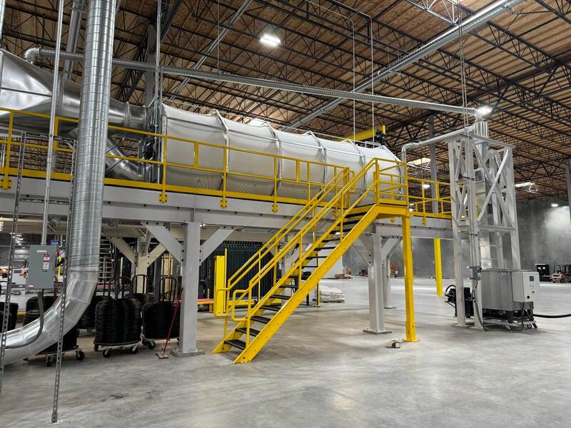 CCM® drum filter installed on a steel mezzanine with a yellow access stair, spiral duct runs feeding it from the plant floor and overhead ducting carrying across the roof