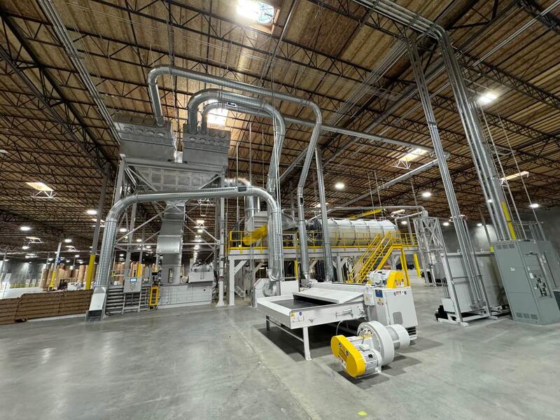 Complete trim removal and dust collection system in a board plant: separators on a steel tower, a CCM drum filter on a yellow-railed mezzanine, a shredder and conveyor fans in the foreground, and paper rolls stored in the background