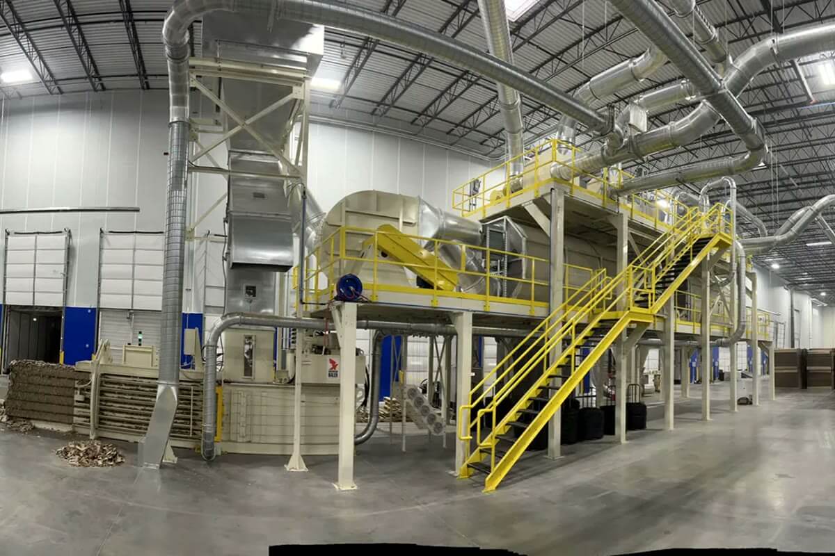 Ducting running across a plant hall to a collector on a mezzanine, with the production line working underneath.